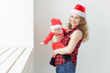 Family, childhood and Christmas concept - Young mother holding baby in santa suit indoor