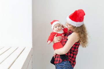 Family, childhood and Christmas concept - Young mother holding baby in santa suit indoor