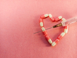 pink medical capsule in the shape of a heart with a syringe on a pink background