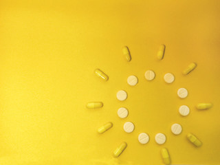 figure of the sun from medical white pills and yellow capsules on a yellow background