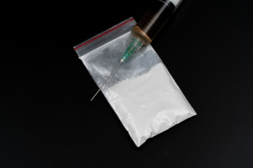 Cocaine or other illegal drugs, white powder, syringe, isolated on black glossy background