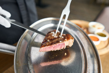 The waiter is holding a plate Grilled striploin steak with Pickled cabbage and two sauces. The strip steak, also called a New York strip. Serving on a wooden Board. Barbecue restaurant menu.