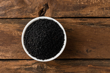 Black cumin seeds in bowl on rustic wooden table. Top view