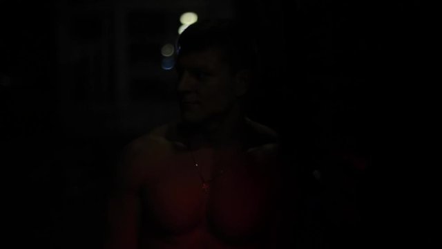 Close view of a handsome shirtless man near a fire truck with flashing lights at night