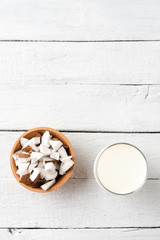 Glass of coconut milk on white wooden background with coconut pieces and copyspace. Top view