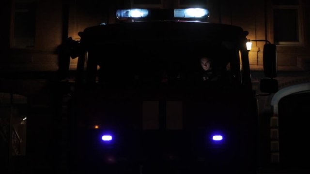 Front of a fire truck with flashing emergency lights and sirens at night. Fireman in front seat