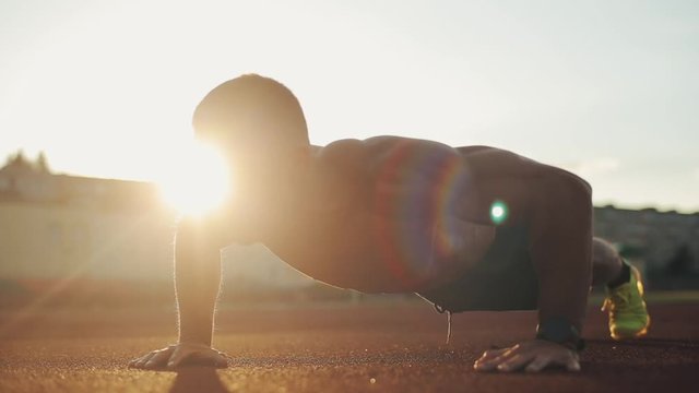 A close-up side view of a young muscular bodybuilder pumping up arms with a barbell