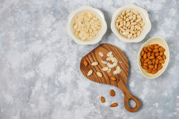 Peeled (blanched) and unblanched whole almonds in ceramic bowls on grey concrete background