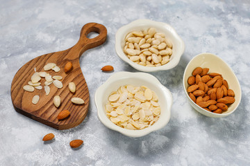 Peeled (blanched) and unblanched whole almonds in ceramic bowls on grey concrete background