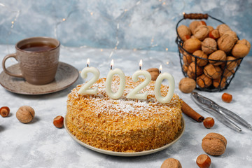 Carrot cake with 2020 candles and a cup of tea on grey concrete background