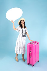 Happy asian tourist with pink luggage and holding white speech bubble board on blue background.