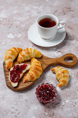 Fresh tasty homemade croissants with raspberry jam on grey-white background. French pastry