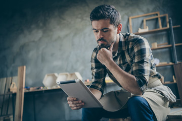 Photo of handsome serious guy holding e-reader website checking email online orders think how to improve service wooden business industry owner woodwork store indoors
