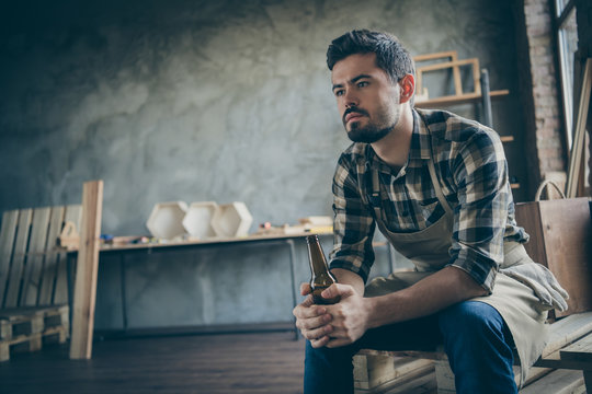 Photo of handsome serious guy holding beer bottle have to work abroad to earn money miss family lonely ending of day wooden business industry woodwork store indoors