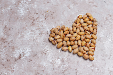Pistachio nuts in shape of heart on concrete background.