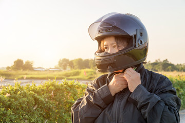 Asian woman with helmet and wearing and fasten before riding big bike motorcycle on the road for safety