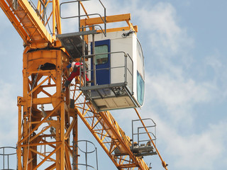 Crane workers in overalls are repairing a high-rise tower crane working during the construction of a multi-storey building. Risky work at height. Lifting heavy building materials. City development.