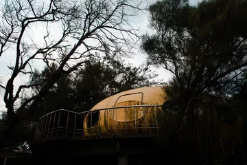 Behangcirkel Abandoned yellow UFO house near tall trees in the evening in Wanli UFO Village, Taiwan © Andrew Haimerl/Wirestock