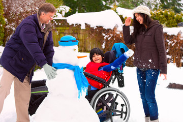 Disabled boy in wheelchair building snowman with family during  winter