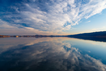 Cumulus clouds on blue sky reflecting at water of Baikal lake after sunset in May