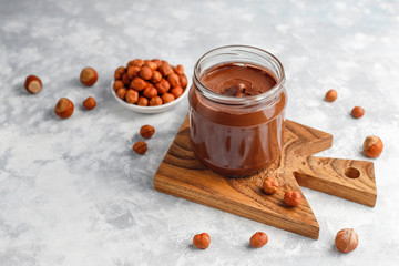 Chocolate spread or nougat cream with hazelnuts in glass jar on concrete background, copy space