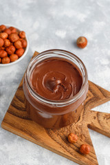 Chocolate spread or nougat cream with hazelnuts in glass jar on concrete background, copy space