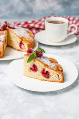 Raspberry cake with powdered sugar and fresh raspberries on a light background. Summer berry dessert.