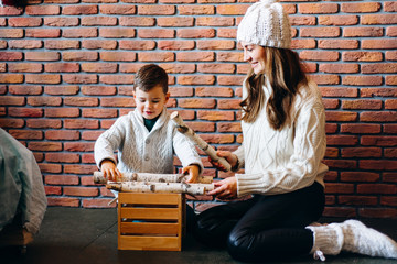 Fototapeta na wymiar Mom with son in knitted sweaters playing, stacking firewood in a drawer. Winter New Year and Christmas mood