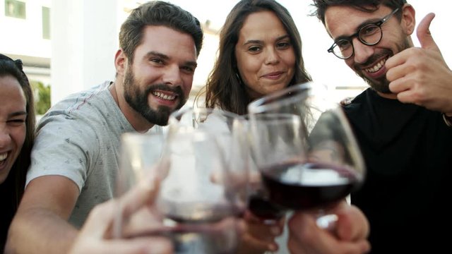 Cheerful friends toasting to camera with glasses of red wine. Cheerful friends posing with red wine for photo. Celebration concept