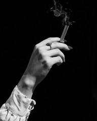 Vertical grayscale shot  of a female hand holding a marijuana blunt on black background - addiction