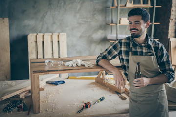 Profile side photo of positive cheerful worker hardwood worker complete his renovation slab table order relax rest hold bottle beer enjoy in house home garage