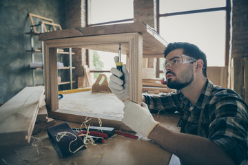 Focused workman in his house home garage repair wooden slab table use screwdriver drill screws wear...