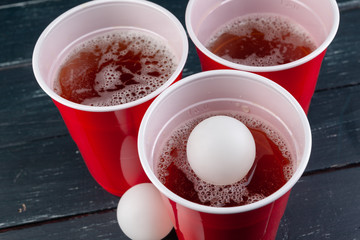 Wooden table with red cups and ball for beer pong