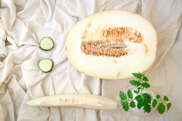 Still life with fresh melon and cucumbers and green twig of tomato plant on white mint. Sunny cheerful mood.