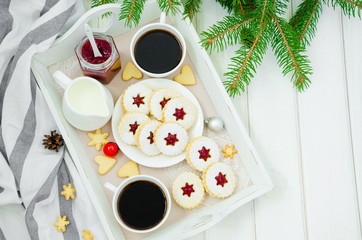 Christmas Linzer cookies filled with strawberry jam on a white plate on a tray with two cups of coffee.  Morning Christmas, Christmas breakfast.