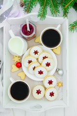 Christmas Linzer cookies filled with strawberry jam on a white plate on a tray with two cups of coffee.  Morning Christmas, Christmas breakfast.