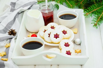 Christmas Linzer cookies filled with strawberry jam on a white plate on a tray with two cups of coffee.  Morning Christmas, Christmas breakfast.