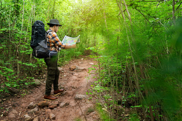 Naklejka premium man traveler with backpack and map searching directions in the forest