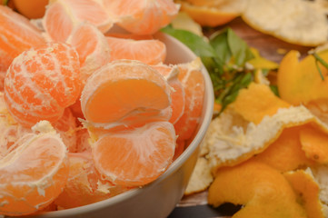 Peeled tangerines in a ceramic dish, tangerine peel on a wooden background. Autumn harvest. Close up.
