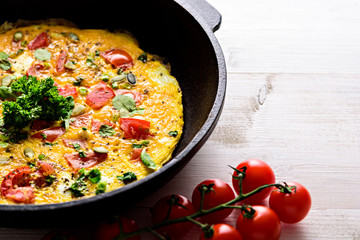 close up scrambled eggs with cherry tomatoes and greens in a cast iron pan on a white background