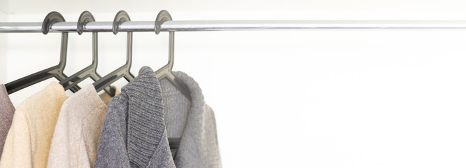 Sweaters and cardigans in grey neutral tone hanging in the store. Warm comfortable clothes for...