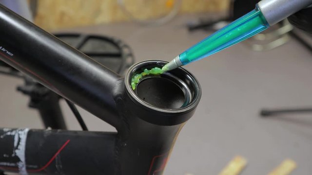 A close up view of greasing bicycle headset bearing. Wearing a black latex glove.