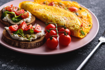 Breakfast with omelet and grain bread with cream cheese, pesto and cherry tomatoes on a pink plate close-up
