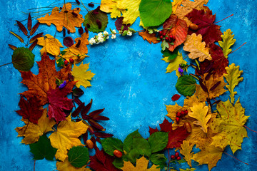 Autumn composition. Wreath of fallen green, yellow, orange and red leaves in a circle on a turquoise background. Autumn, leaf fall,. Flat position, top view, copy space