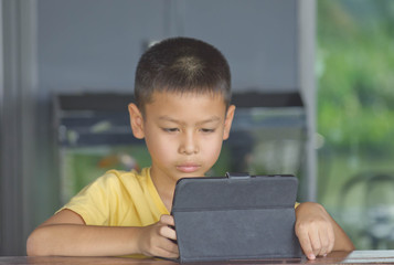 Portrait of Asian boy playing mobile phone on wooden table.