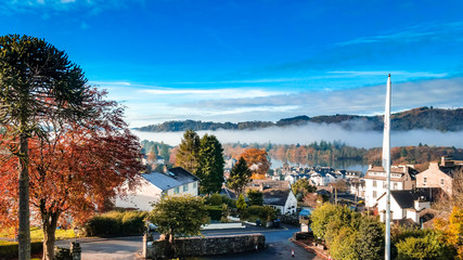 Aerial top view over Bowness On Windermere on an early morning with fog and mist rising on lake Windermere. Autumn in the Lake District, Cumbria, UK.  - obrazy, fototapety, plakaty