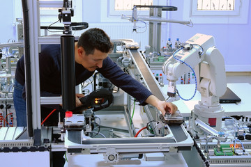 industry 4.0 concept: A mechatronics engineer is holding product and teaching robot arm the positions with teach pendant on smart factory production line background. Selective Focus.