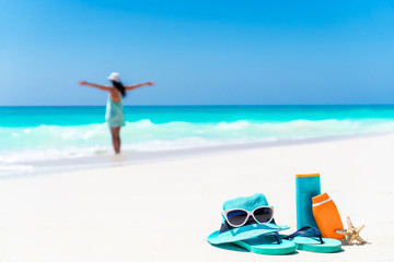 Suncream bottles, sunglasses, flip flop on white sand background ocean