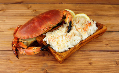 Whole fresh cooked brown crab and fresh meat in a wood dish on a wooden background with lemon and salad leaves © philip kinsey