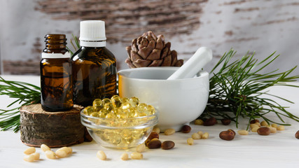 composition of cedar oil with pine nuts on a background of a branch with a pine cone, on a light wooden background